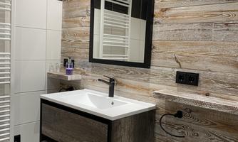A modern bathroom with wooden paneling and an elegant sink. The large mirror reflects the stylish decor.