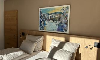 A cozy bedroom with two beds and a wooden wardrobe. A colorful painting hangs on the wall.