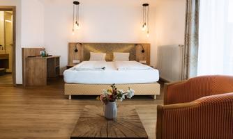 A modern bedroom with a large bed and a cozy sitting area. Soft colors and natural materials create an inviting atmosphere.