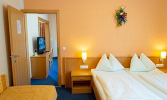A cozy hotel room with two single beds and orange walls. In the background, there is a television and tasteful decor.