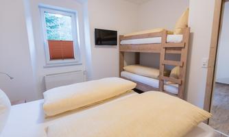 A cozy room with a double bed and a bunk bed. There is a window with a roller shutter and a television on the wall.