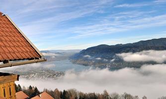 A picturesque view of a lake, surrounded by mountains and mist. The sky is clear and blue, with soft clouds on the horizon.