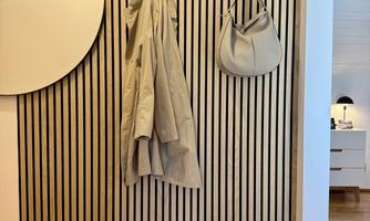 A modern wall with vertical stripes, a round mirror, and a beige coat. A handbag is hanging right next to it.