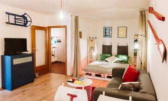 A cozy apartment with a sleeping area, a sofa, and modern furnishings. Decorative elements hang on the wall, giving the space an inviting atmosphere.