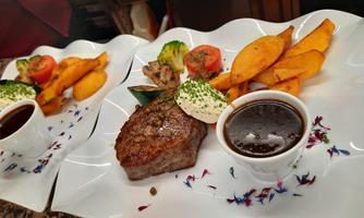 A delicious dish with perfectly cooked steak, side dishes of vegetables and potatoes. In addition, there is a tasty sauce in a small bowl.