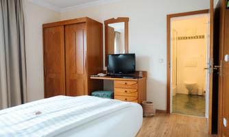A simple hotel room with a bed, a desk, and a television. In the background, access to the bathroom is visible.