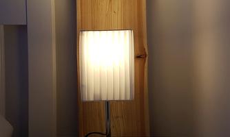 A bedside table with a lamp and an open book. In the background, a wooden board is visible.