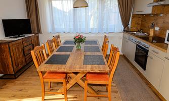 A cozy dining area with a large wooden table and chairs. The kitchen is modern and bright, featuring a decorative bouquet in the center.