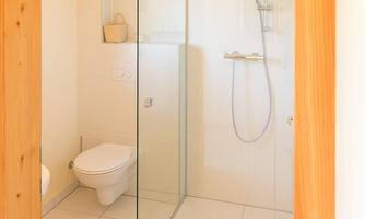 A modern bathroom with a glass shower cabin and bright tiles. A colorful rug is on the floor.