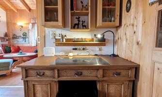 A cozy wooden desk with two drawers stands in a warm, rustic environment. Above are wooden shelves with decorative elements.