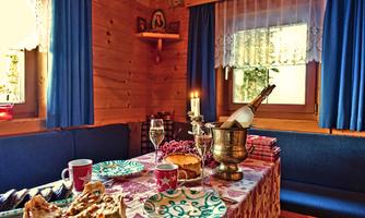 A festively set table in a cozy wooden cabin. There are champagne, cake, and decorated plates.