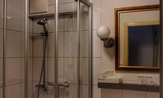 A modern bathroom with a glass shower cabin and a wooden ceiling. The sink area is equipped with a large mirror and a wooden shelf.