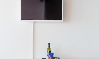 A bright dining area with a white table and red chairs. A television is mounted on the wall.