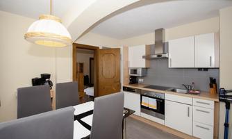 A modern kitchen with white cabinets and a dining table. The equipment includes a stove, a hood, and various kitchen appliances.