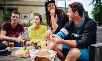 A group of friends is enjoying a meal outdoors. They are laughing and chatting comfortably over drinks and snacks.