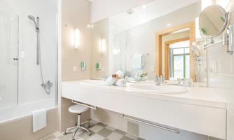 A modern bathroom with a bathtub and sink. It has bright colors and large mirrors that make the space look friendly and inviting.