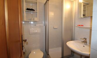 A small bathroom with a shower, a sink, and a toilet. The walls are tiled and there are practical storage options.
