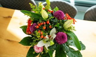 A colorful bouquet with various flowers in different colors. The bouquet is lying on a wooden table and brings a cheerful atmosphere.
