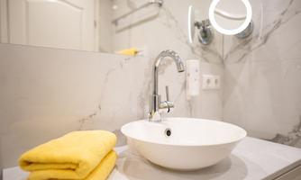 A modern bathroom with a white sink and an elegant faucet. Next to the sink, yellow towels are lying on the countertop.