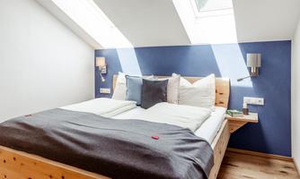 A modern room with a large bed and stylish pillows. A lot of daylight streams into the room through the skylights.