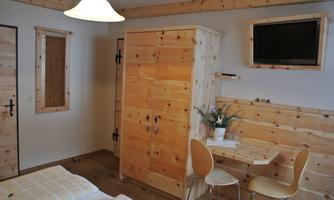 A cozy room with wooden furniture, a table and chairs. There is also a small television and a bright lamp.