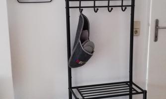 A black clothing rack with several hooks and a mirror. Below it is a shoe shelf and a small troop.