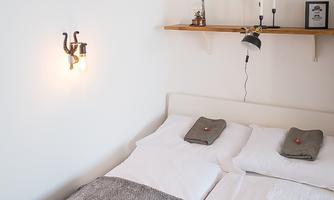 A cozy bedroom with a double bed and a warm, neutral color scheme.  
On the wall is the word "LOVE" and a simple shelf with candles.