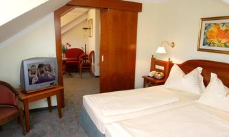 A cozy room with two beds and wooden details. In the background, there is a seating area with a television and a door to another room.