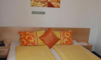 A bright bedroom with two single beds and orange-yellow bedding. A piece of artwork hangs on the wall, creating a cozy atmosphere.