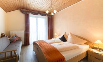 A bright and cheerful bedroom with two beds and a sofa bed. Large windows provide plenty of natural light and a view outside.