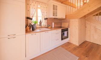 A modern kitchen with white cabinets and a wood stove. The light falls through a window, creating a cozy atmosphere.