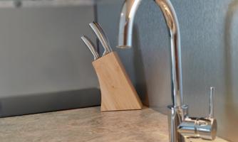 A modern kitchen sink with an elegant faucet and a wooden knife block. The surface is made of light material and conveys a clean, tidy atmosphere.