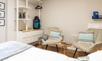 A cozy room with two armchairs and a small table. In the background, a coat rack and a backpack can be seen.