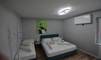 A simple room with two single beds and modern, minimalist furniture. A green picture hangs on the wall, and the room is bright and well-lit.