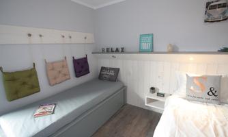 A cozy bedroom with a bed and a seating area. Decorative pillows hang on the wall along with a sign that says "RELAX".