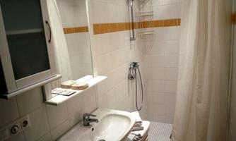 A small, modern bathroom with white walls and orange accents. There is a shower, a sink, and a mirror.