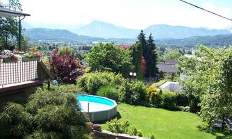 A beautiful garden with a pool and lush vegetation. In the background, mountains and a blue sky can be seen.