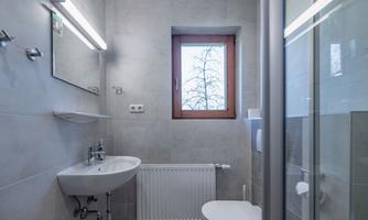 A modern bathroom with gray tiles and a sink. A window lets in daylight and offers a view of trees.