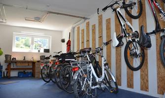 A modern garage with several bicycles, some hanging on the wall and others standing on the floor. The space has a bright, tidy impression with a window that lets in daylight.