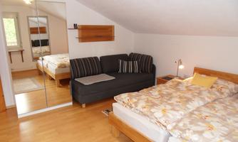 A cozy bedroom with two single beds and a couch. The room has a warm wooden floor and a large mirror.