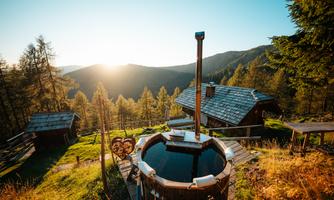A dreamlike view of the mountains at sunrise. In the foreground stands a wooden bath with inviting water.