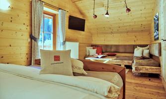A cozy room in a wooden house with a double bed and a seating area. Large windows let in plenty of light and create a relaxed atmosphere.
