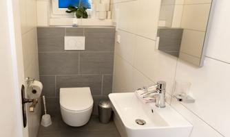 A modern bathroom with bright tiles and a small window. A toilet, a sink, and toilet paper are visible in the corner.