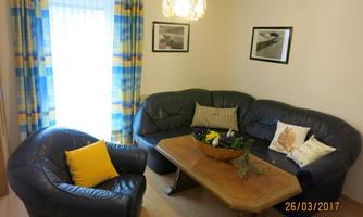 A cozy living room with a dark blue couch and a wooden table.  
Large windows with colorful curtains provide natural light.