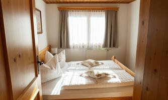 A cozy bedroom with a double bed and wooden details. Brightness flows through the window with curtains.