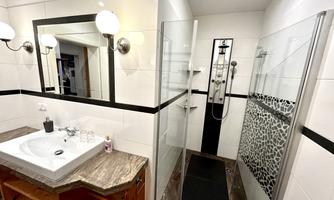A modern bathroom with a shower and a sink. The walls are white tiled with black accents and decorative elements.