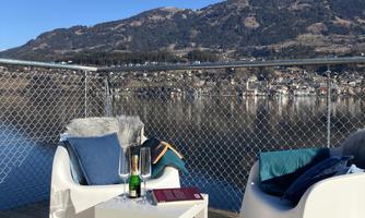A cozy seating area on a terrace overlooking a lake and the surrounding mountains. The table is decorated with champagne and glasses.
