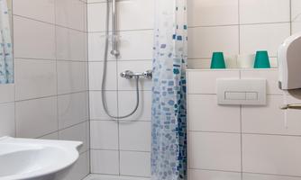 A modern bathroom with a shower, sink, and toilet. The walls are light-tiled and the furnishings are functional.