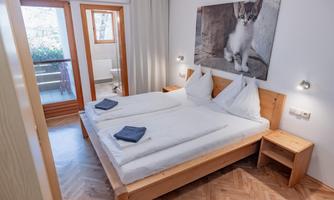 A cozy bedroom with two single beds and wooden wardrobes. A picture of a cat hangs on the wall, and the room has access to a small balcony.