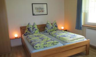 A cozy bedroom with a double bed and colorful bedding. There is soft lighting and a window with a view.